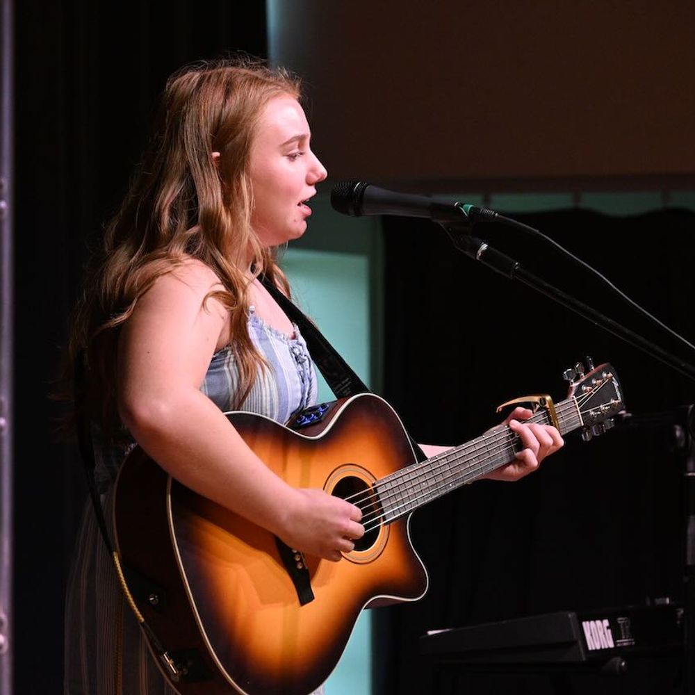 Maddie Connor performing on stage with acoustic guitar