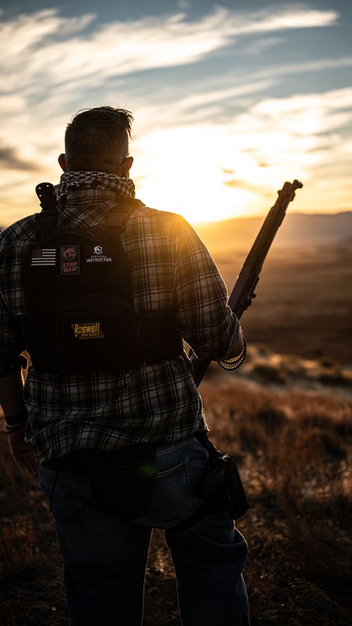 One of the instructors holding a shotgun standing on a hill in front of a sunset