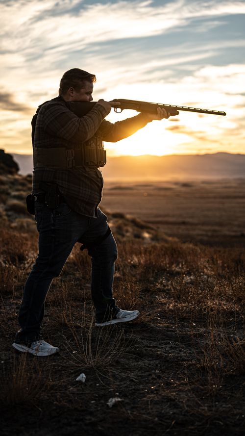 a professional photo of a treasure valley shooting academies range safety officer holding his shotgun in front of a sunset