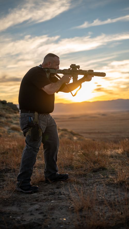 One of the instructors holding a rifle standing on a hill in front of a sunset