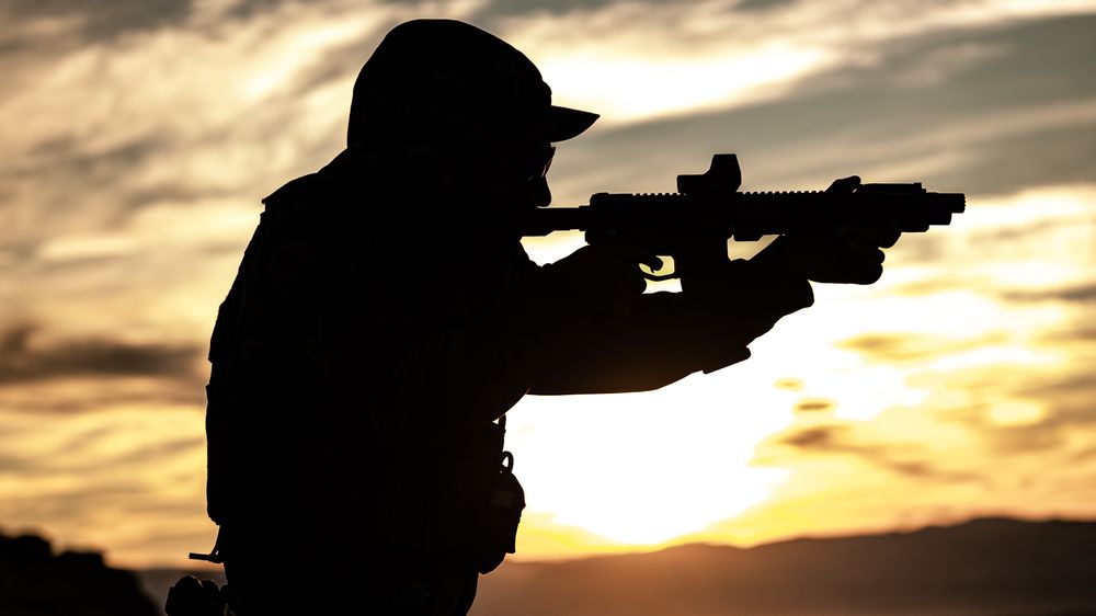 a silhouette photo of one of the instructors holding a rifle with the sun setting in the background