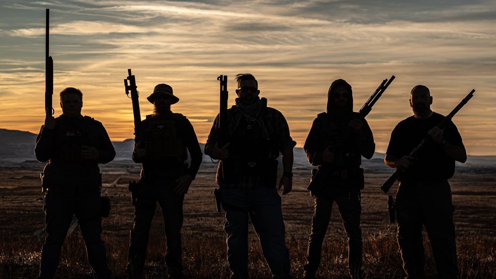 The men of treasure valley shooting academy posing with their shotguns as silhouettes with their backs toward the camera as the sun goes down