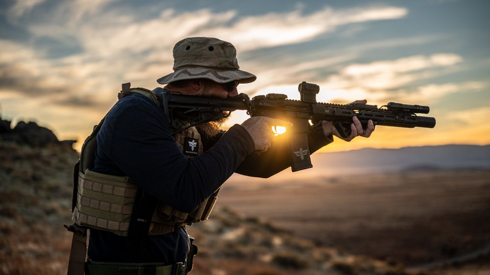 One of the instructors holding a rifle standing on a hill in front of a sunset