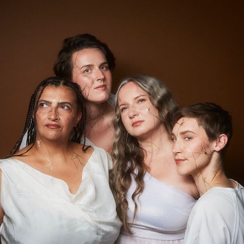 Group portrait of Medusa Quartet against a warm brown background, wearing modern Greek-inspired garments with kintsugi-style gold makeup.