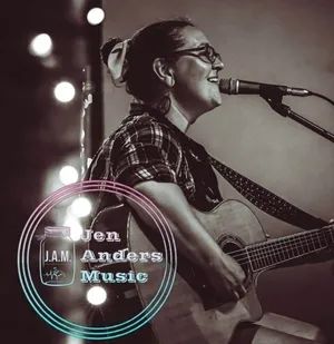 Black-and-white portrait of Jen Anders performing with acoustic guitar.
