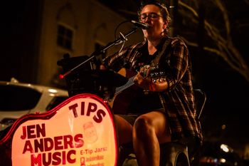 Jen Anders singing and playing acoustic guitar on stage.
