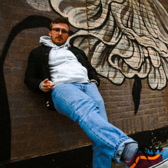 Codey Lee James stands in front of a graffitied brick wall.