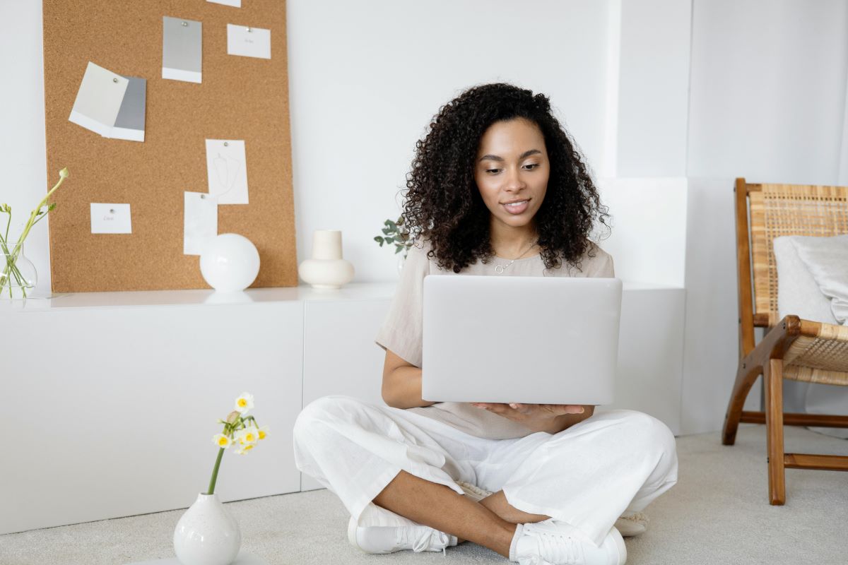 A woman seated on the floor holding her laptop.