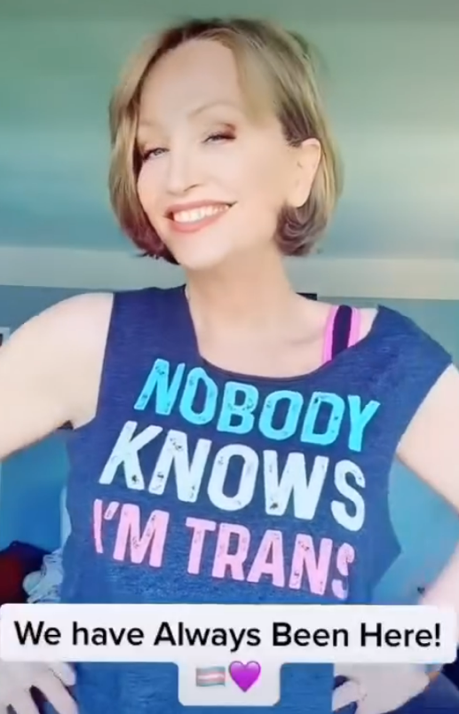 A person smiling with a blue shirt with text on it

Description automatically generated