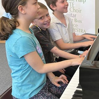 three Music for Young Children students playing the piano and smiling