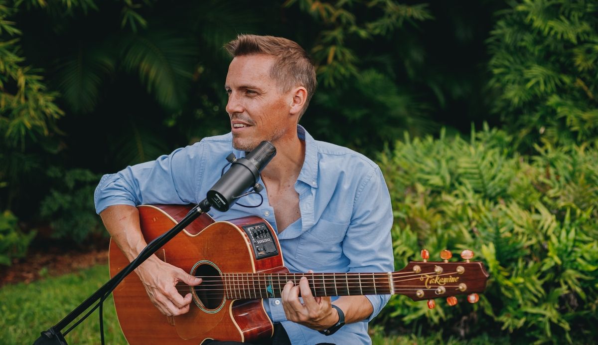 Jonny Leyland singing with acoustic guitar outdoors