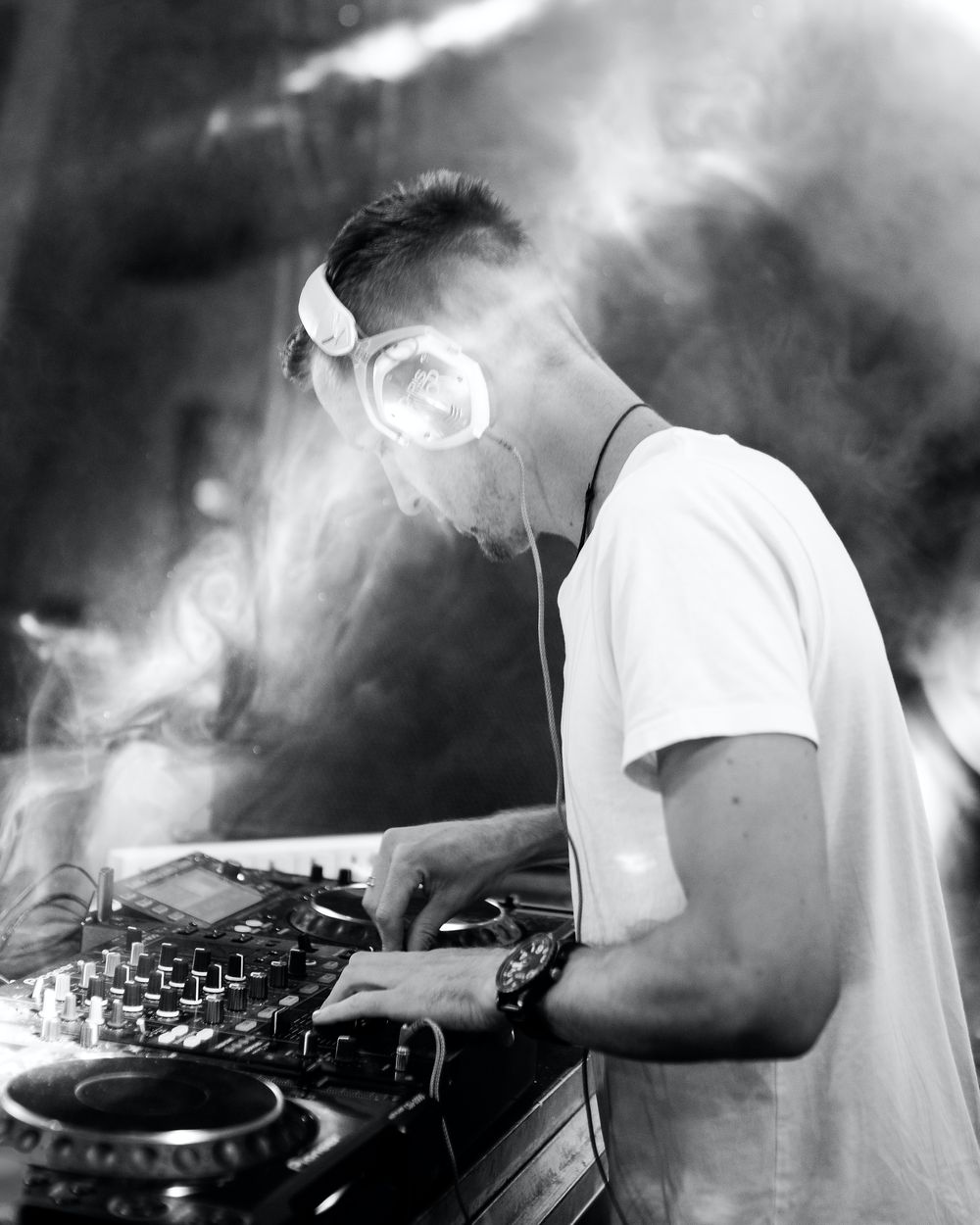 A DJ working the controls of a his DJ turntable. Smoke drifting towards his face.